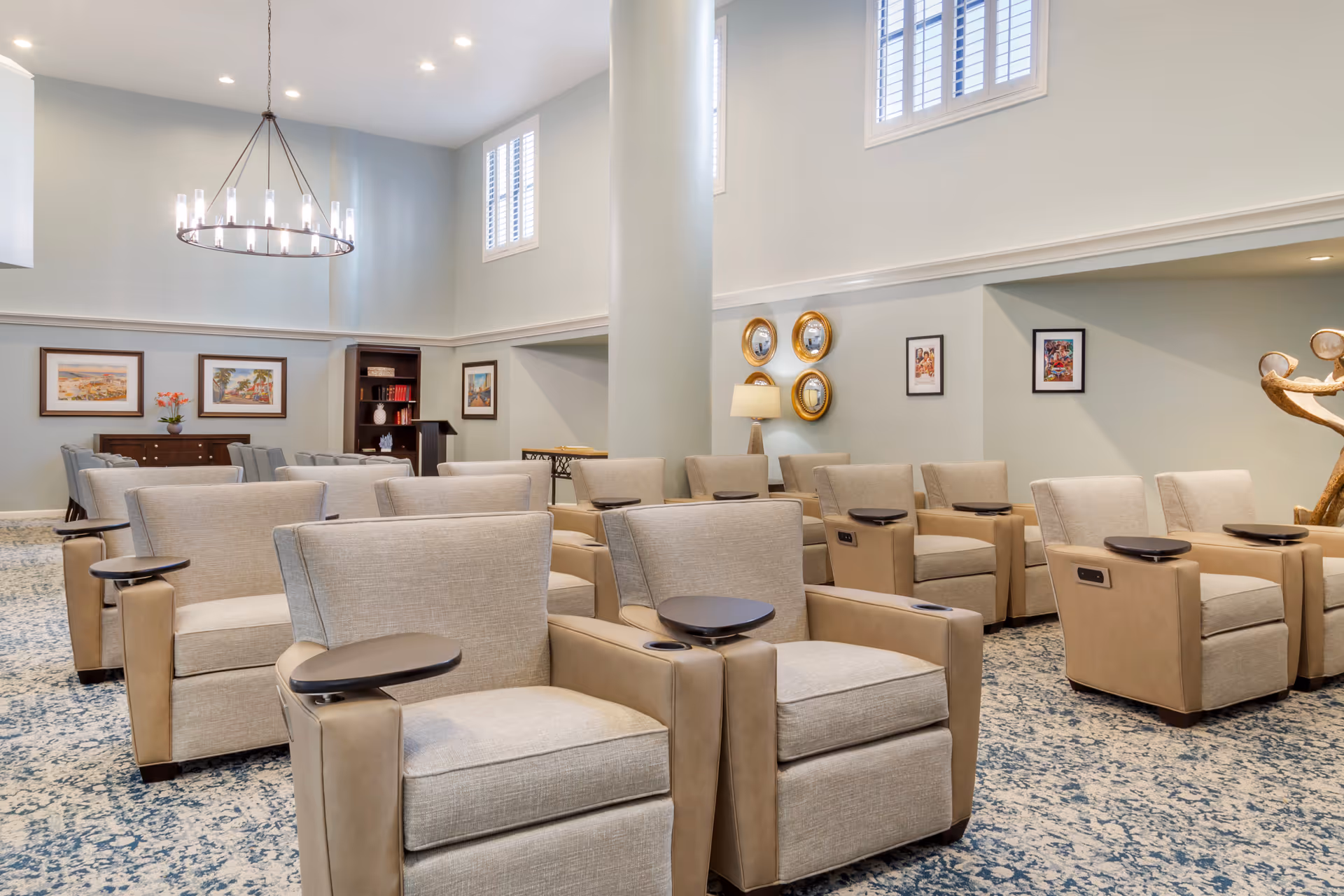 A bright communal lounge with rows of beige reclining chairs arranged in a spacious, high‑ceilinged room.