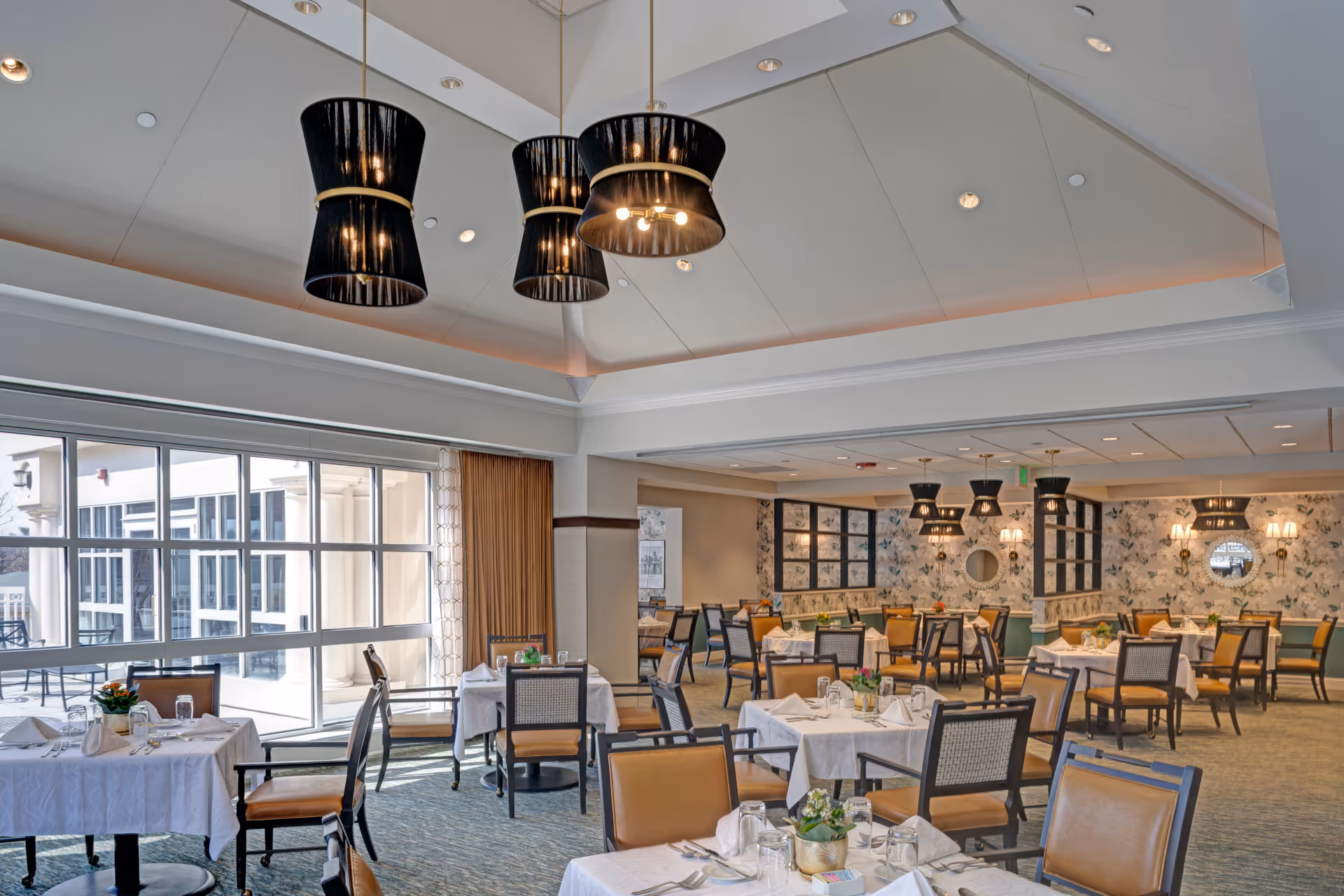 Bright, spacious dining room with multiple set tables and chairs, large windows, and black pendant lights.
