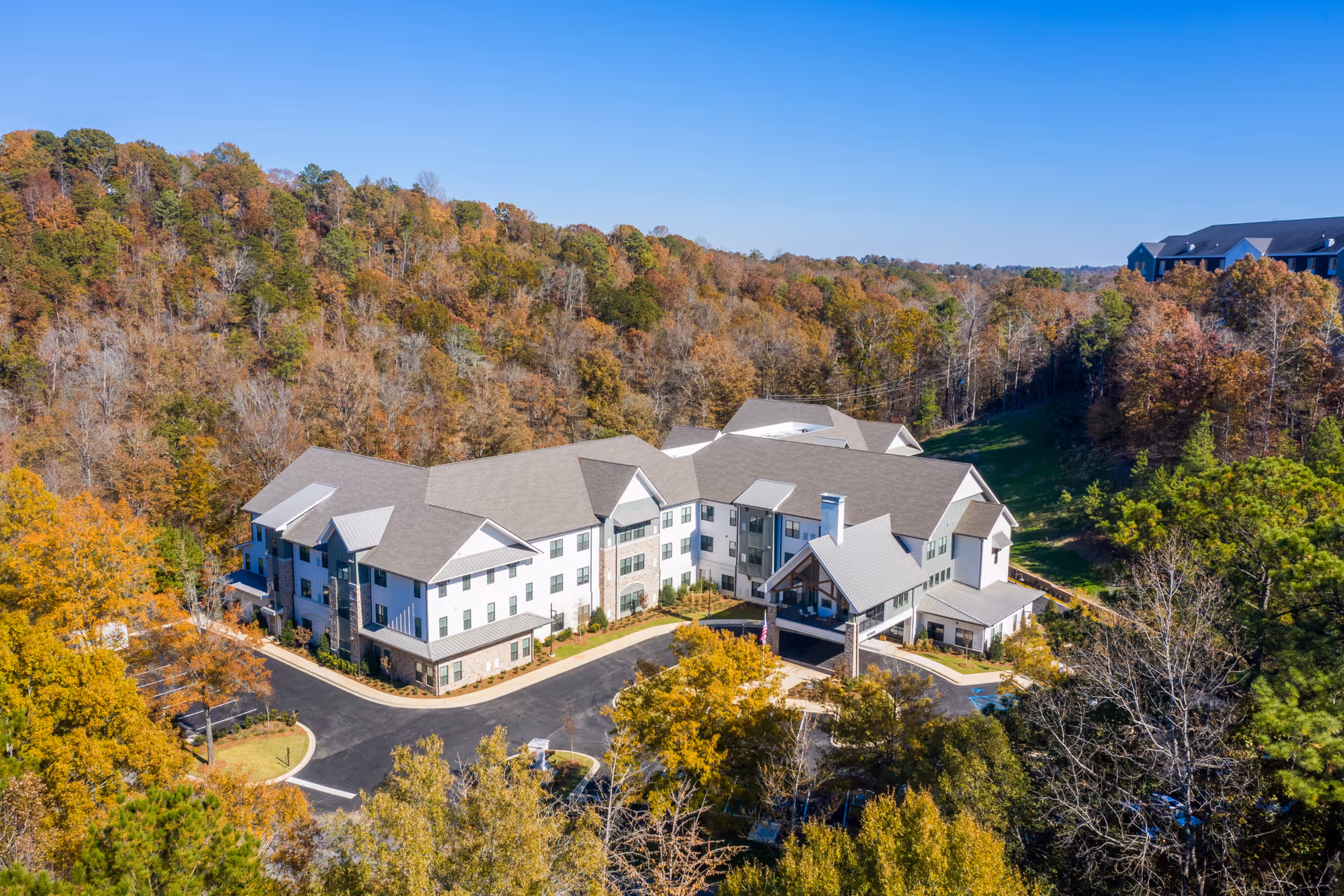 Aerial view of Longleaf Liberty Park senior living facility surrounded by trees with autumn foliage, showing a large multi-story building with a covered entrance and a parking area.