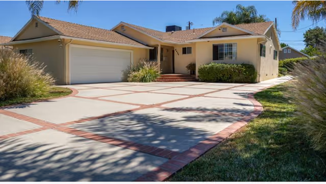 Front exterior of a single-story beige senior living facility with a curved brick-edged driveway and shrubs.