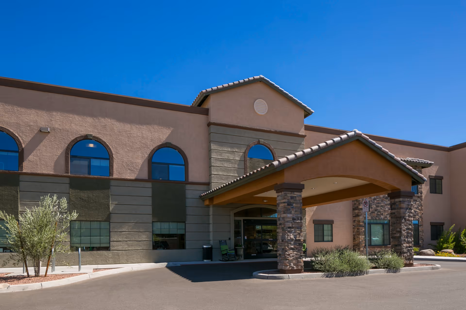 Entrance and porte-cochère of a two-story stucco building with arched windows and stone columns under a clear blue sky.