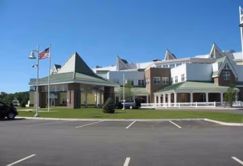 Front exterior view of Merrimack County Nursing Home with parking lot and flag.