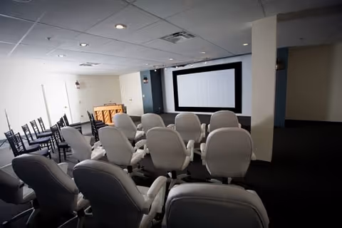 Small screening room with rows of cushioned recliner chairs facing a large projection screen.