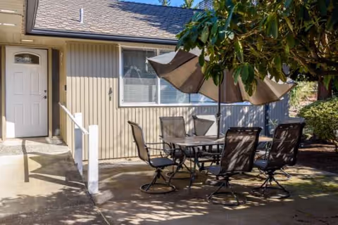 Outdoor patio with table, chairs, and umbrella outside a senior living unit.