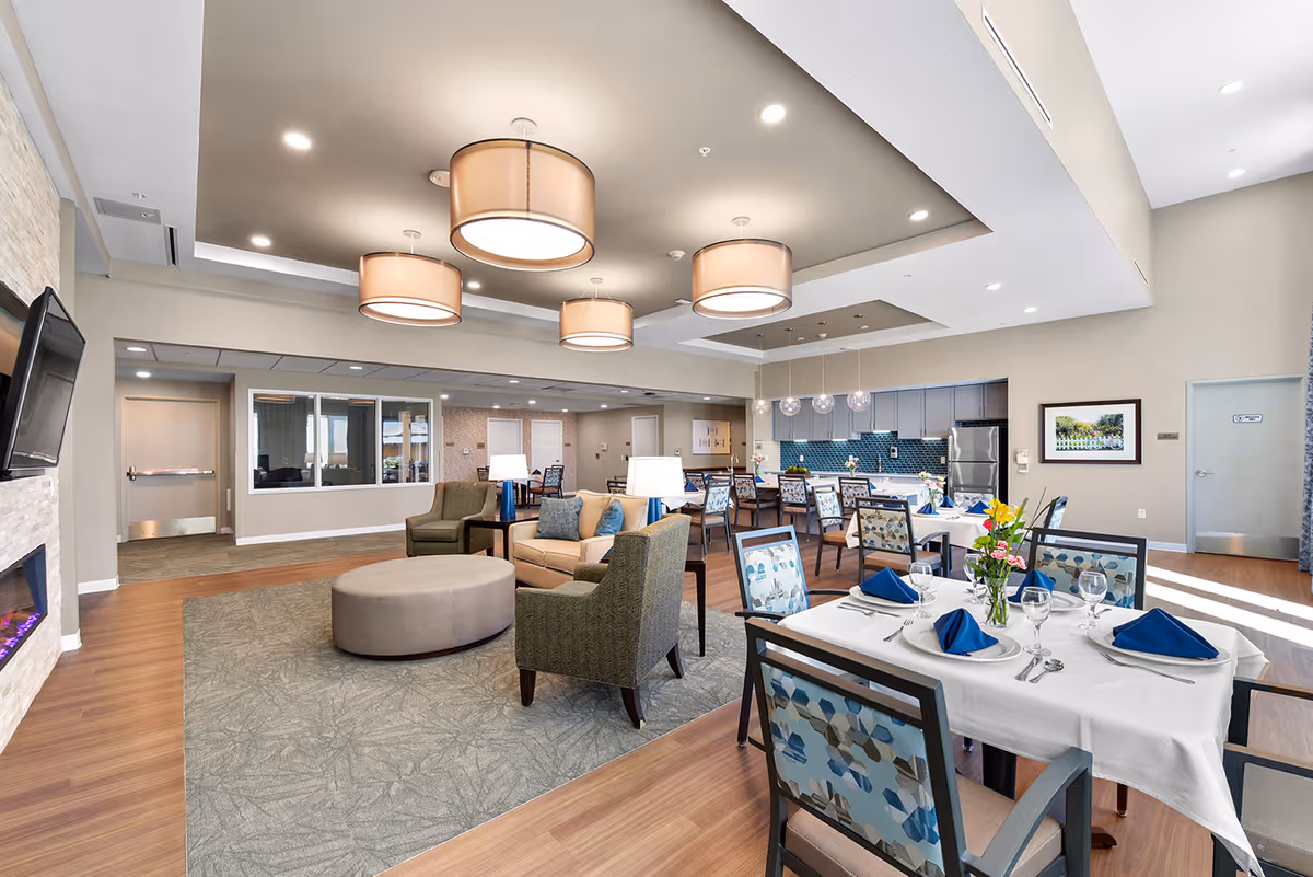 Bright communal dining and lounge area with set dining tables, armchairs, and modern pendant lighting.