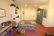 Living room with floral sofa, coffee table, shelves, and warm red carpet in a senior facility.