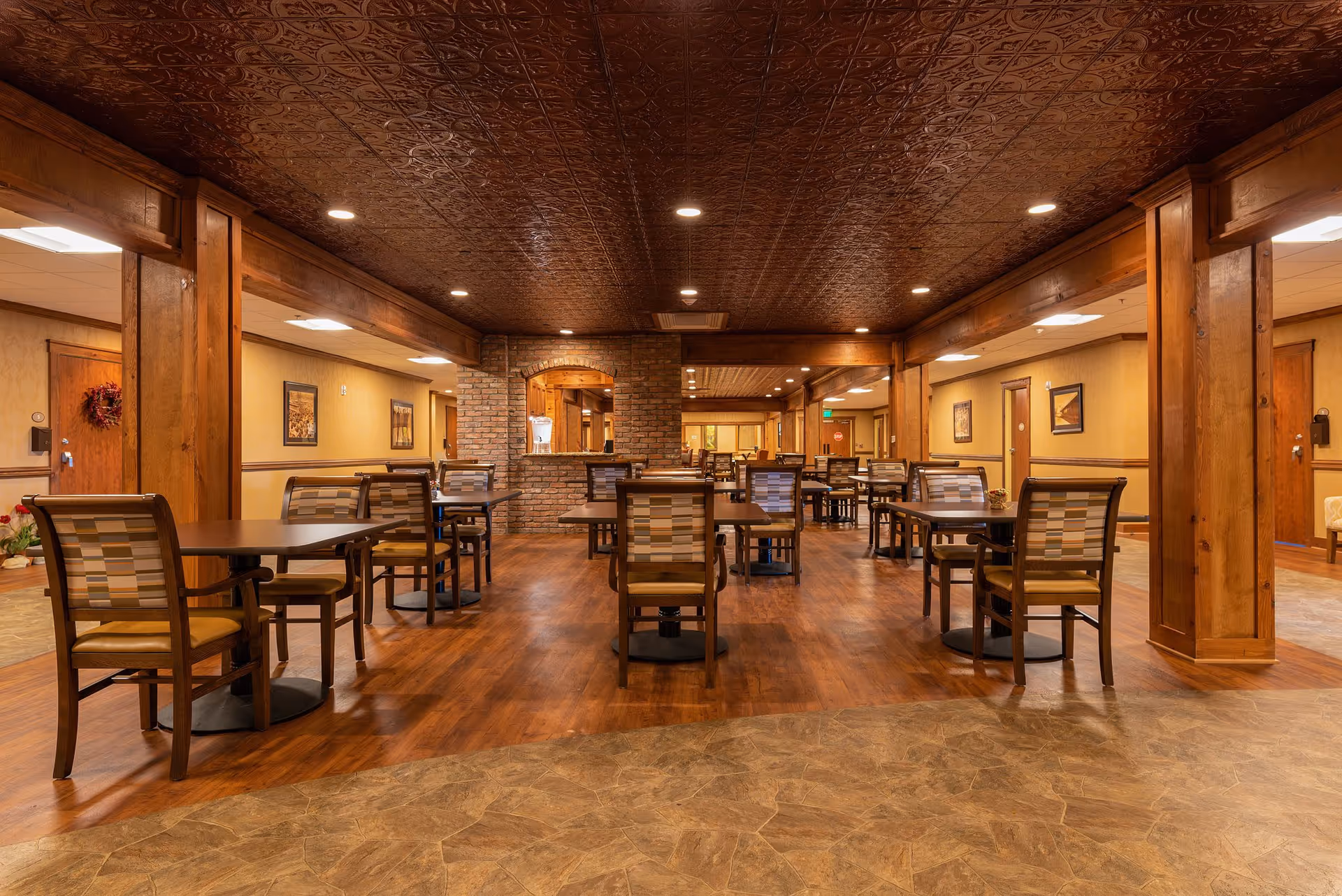 Dining room with rows of tables and chairs, a brick service arch, and warm wood finishes.