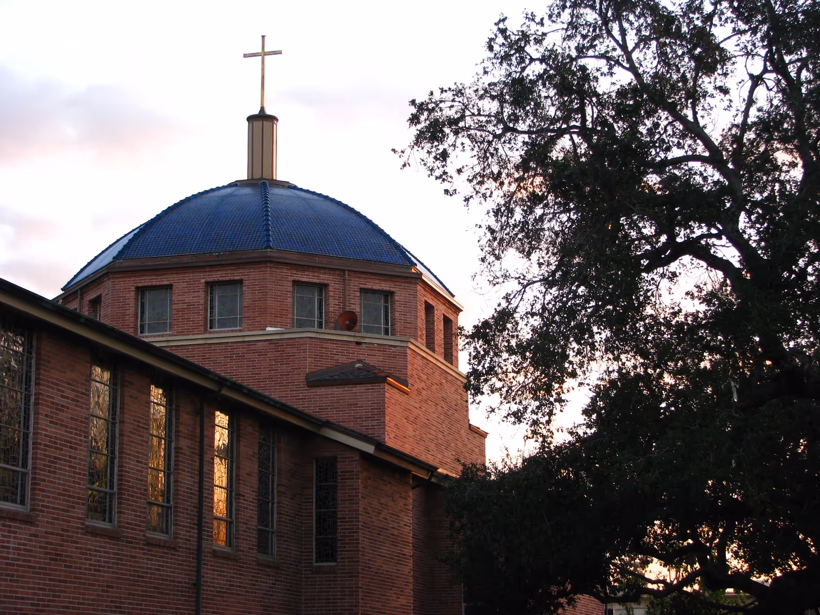 Brick building with a blue domed roof and cross, flanked by trees at sunset.