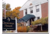 Exterior view of Devereux House, a brick building with white columns and a green awning over the entrance. There is a sign in front that reads 'Devereux House, a Devereux Skilled Care Society' with autumn trees in the background.