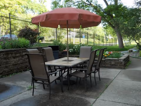 Outdoor patio with a brown umbrella over a square table and six chairs.