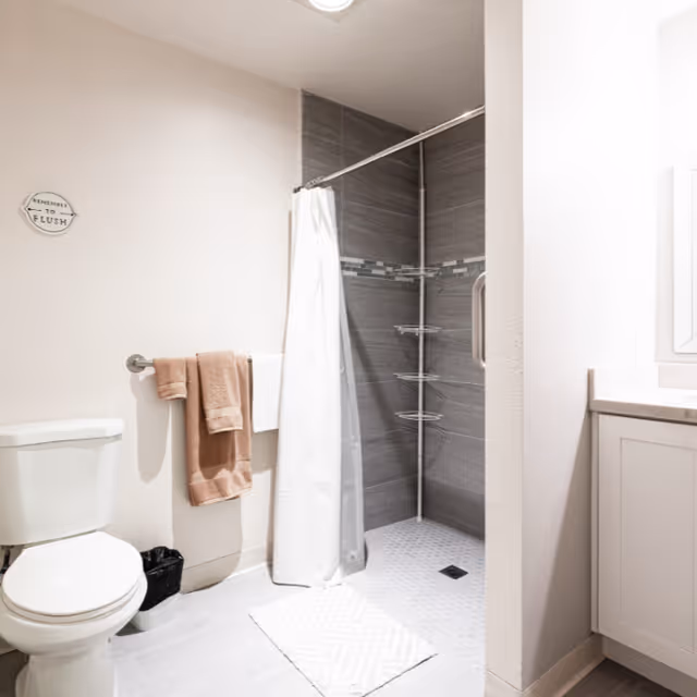 Bright bathroom with a toilet, towel rack, and a tiled walk-in shower with a white curtain.