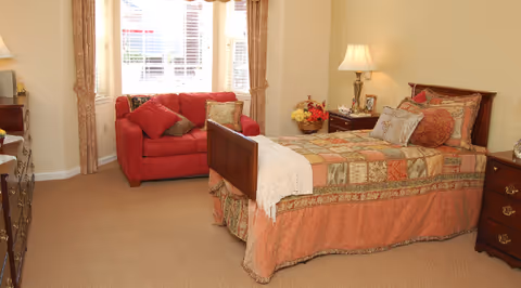 Cozy furnished bedroom with a single bed, nightstand and a red loveseat by a window.