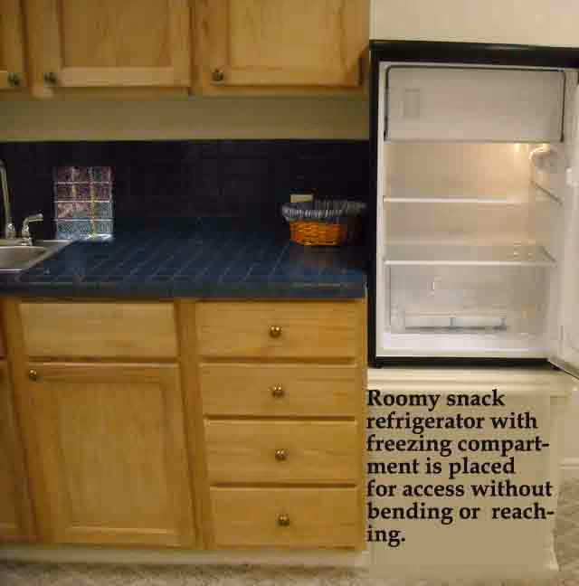 Small kitchen area with wooden cabinets, a blue tiled countertop, a sink, and an open compact refrigerator.