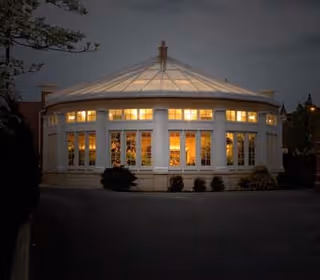 Dusk exterior view of a round glass-walled pavilion at Homeland Center illuminated from within.