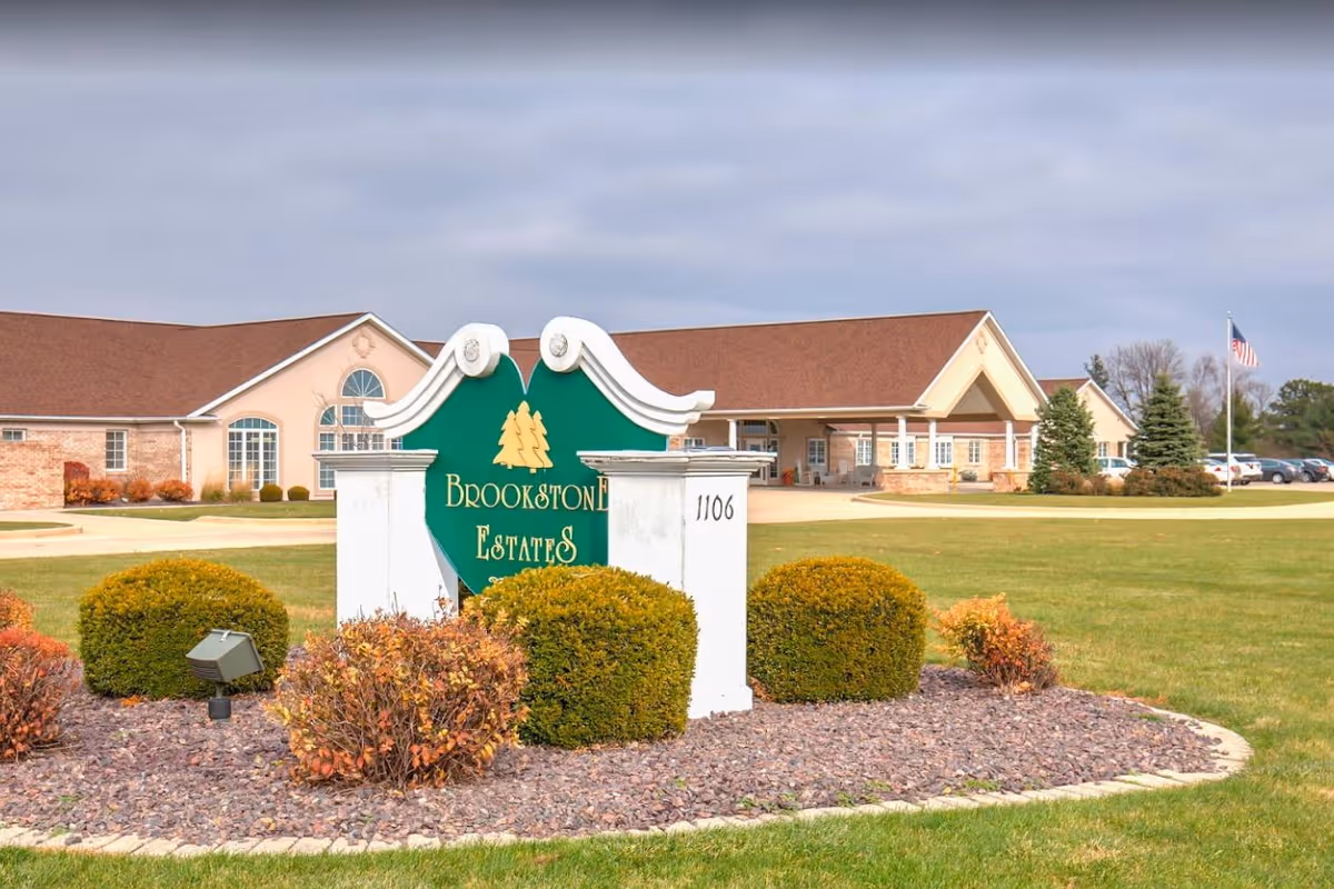 Landscaped entrance sign reading "Brookstone Estates" in front of a single-story senior living building and driveway.