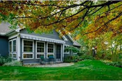 Exterior view of a residential building with a screened porch, surrounded by green grass and trees with autumn-colored leaves.