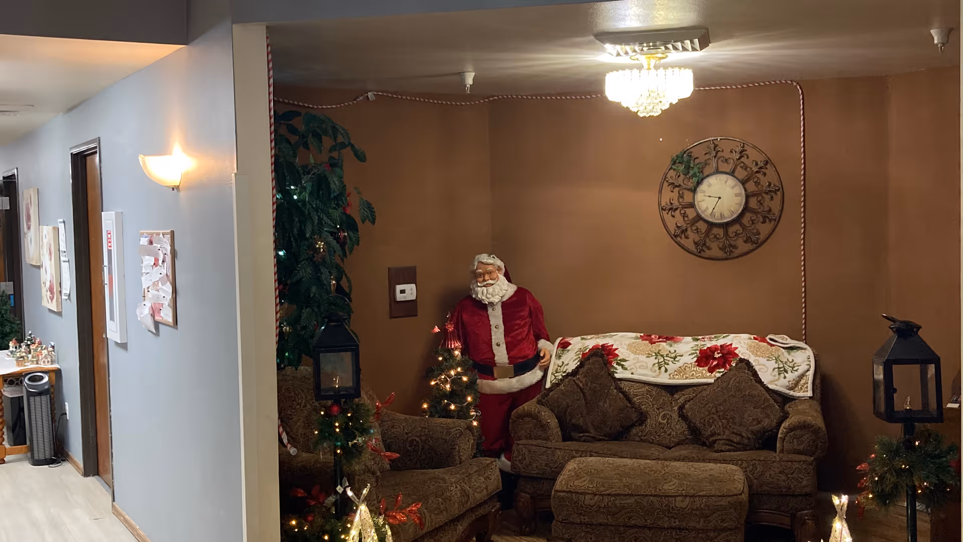 A cozy lounge area with a sofa and chairs decorated for Christmas, a standing Santa figure, and a wall clock.