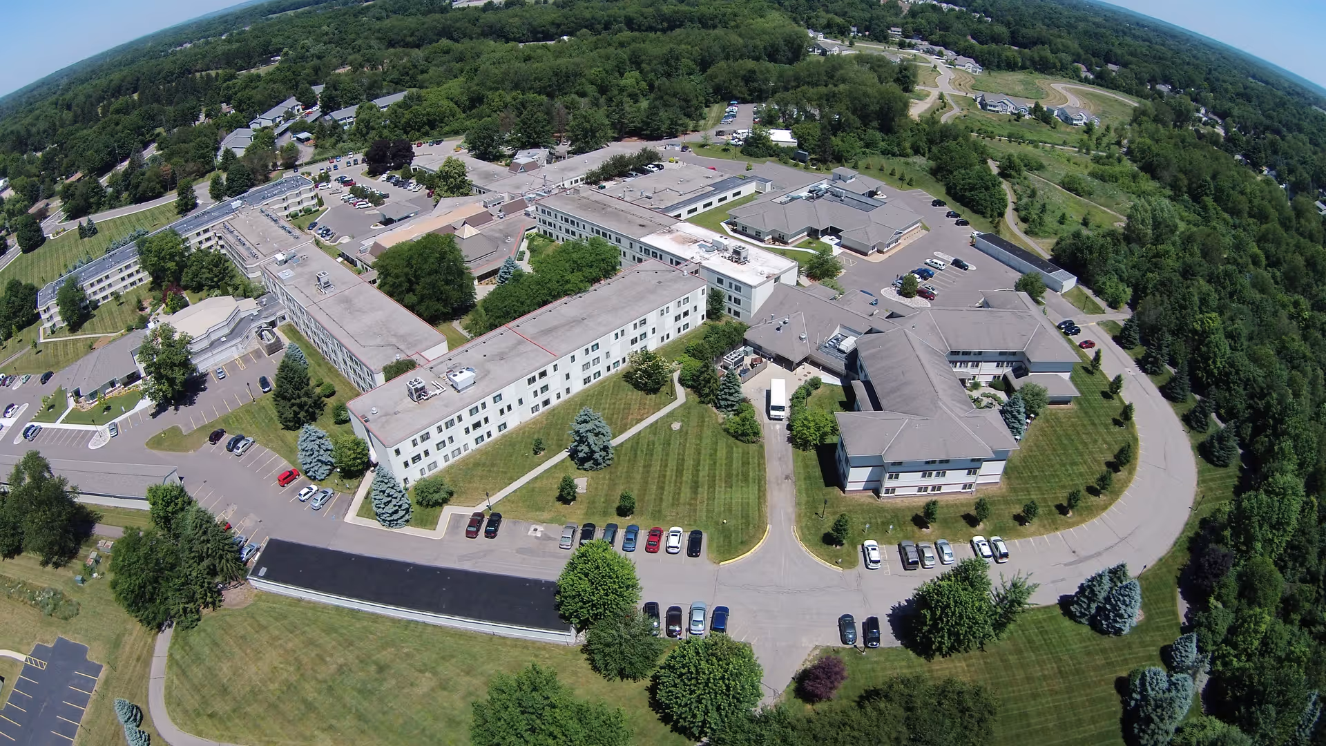 Aerial view of Friendship Village Kalamazoo campus showing multiple connected buildings, parking lots, lawns and surrounding trees.