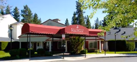 Senior living facility entry with a red awning and landscaped front exterior.