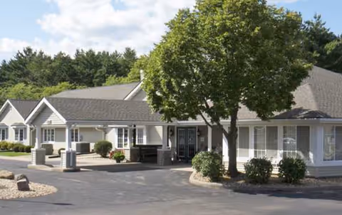 Front view of a single-story Pines Assisted Living building with trees and parking.