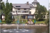 Front view of a large senior living building beside a pond with a fountain