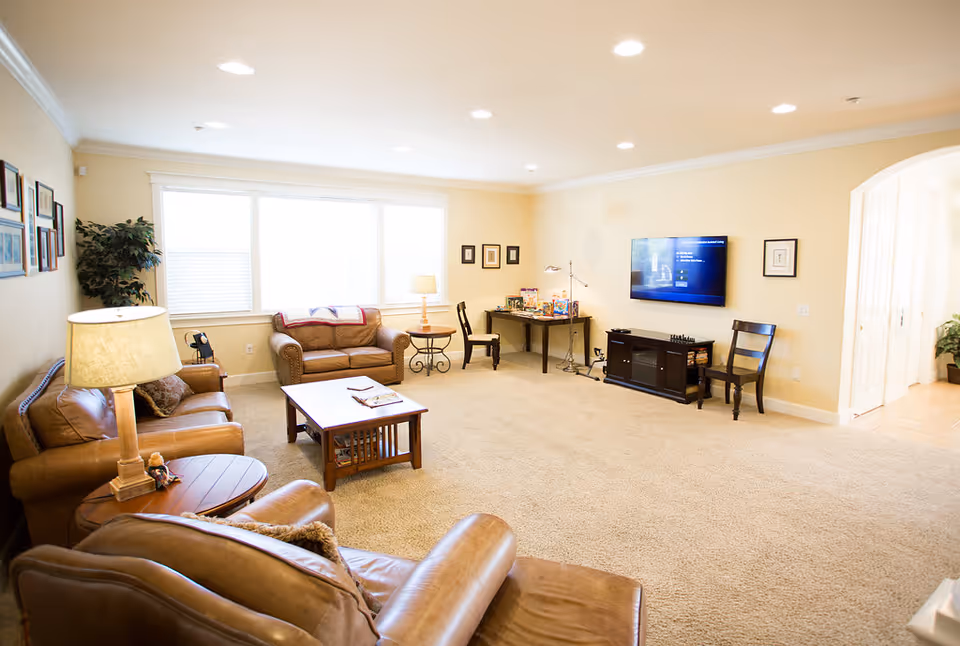Cozy senior living room with leather sofas, coffee table, and a wall-mounted TV.