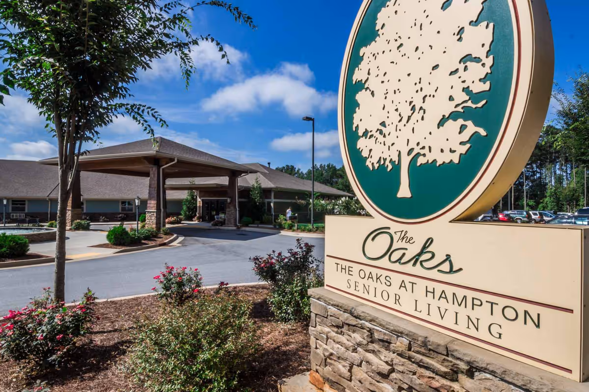 Entrance and large sign for The Oaks at Hampton senior living, with landscaped driveway and covered drop-off.