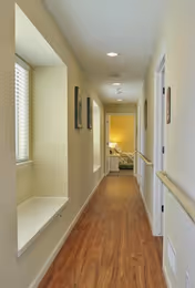 A well-lit interior corridor with wood flooring, handrails, window seats, and a bedroom visible at the far end.