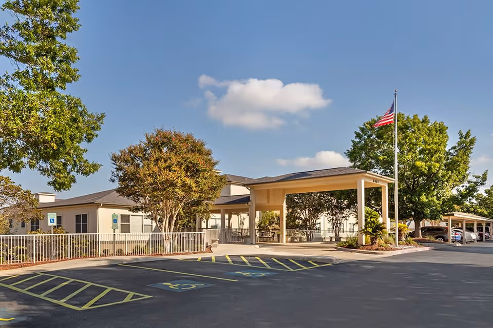 Exterior view of Brookdale Hamilton Wolfe entrance with parking, flag, and blue sky.