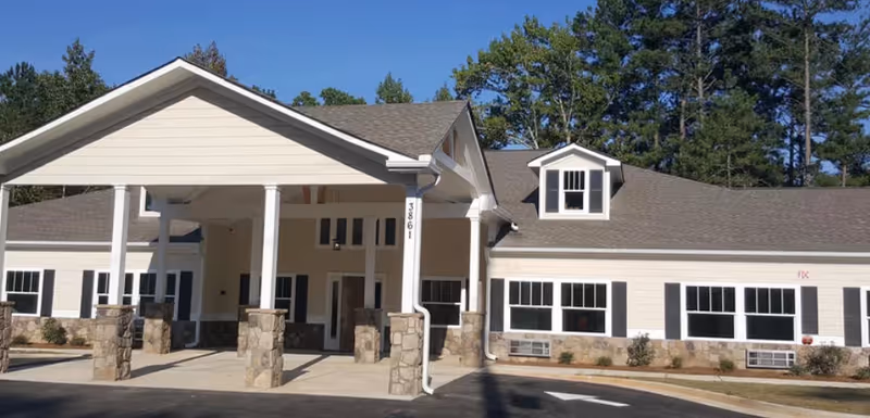 Front entrance of a single-story senior care building with a covered portico supported by stone columns and rows of windows.