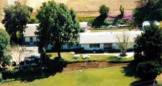 Aerial view of a single-story building surrounded by trees and greenery, with a grassy area and some outdoor seating in front. The building is part of a facility named COUNTRY ROSE ESTATE MEMORY CARE.