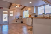 Open communal kitchen area with granite countertop, white cabinets, wood flooring, windows, and an exterior door.