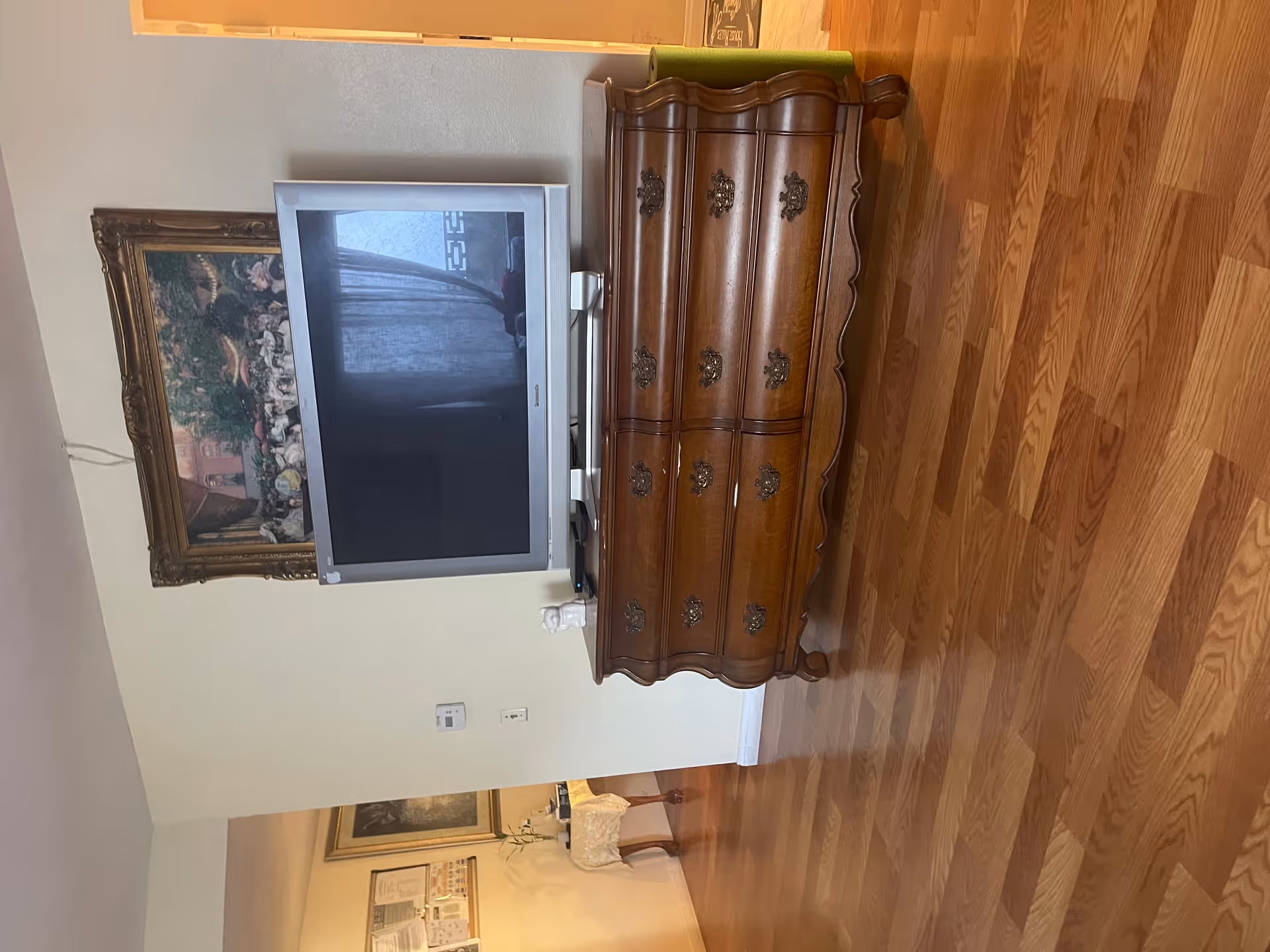 A wooden dresser beside a TV in a living room with framed art on the wall.