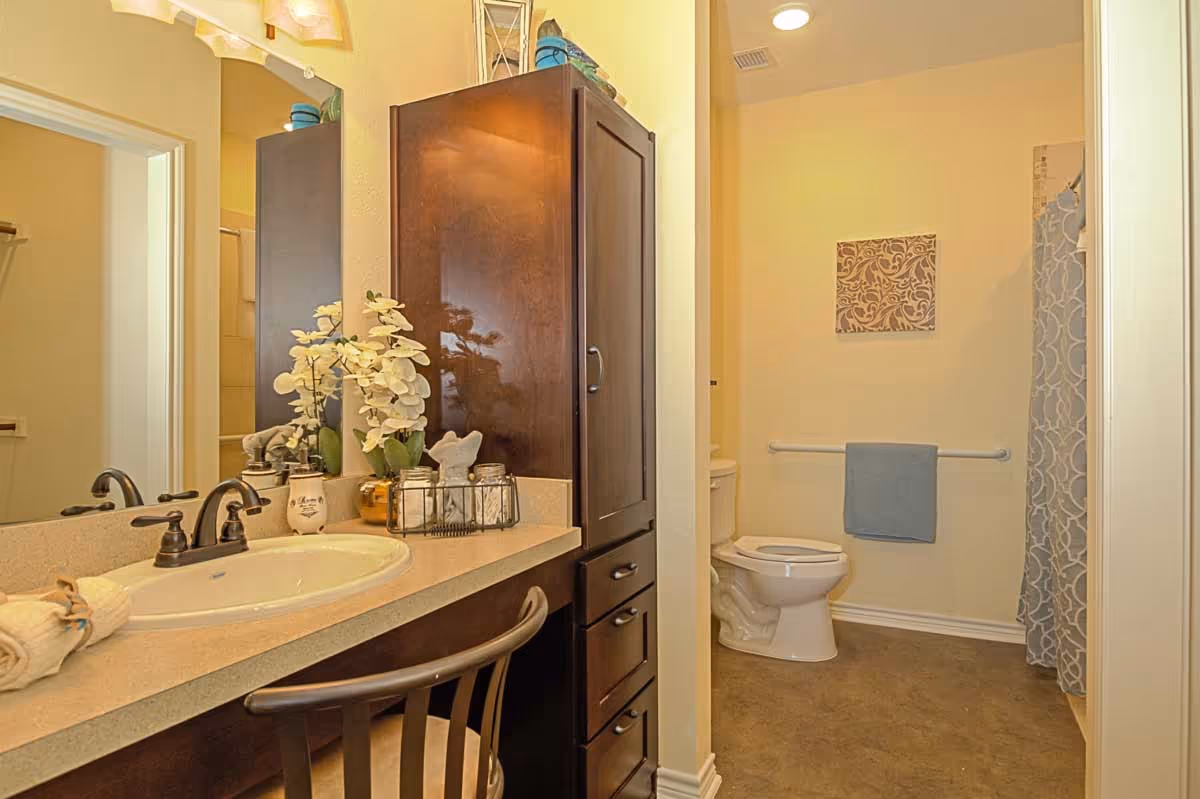 Bathroom with a sink and vanity with flowers on the left, and a toilet and shower with a towel rack on the right.