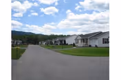 Street view of a row of single-story homes with lawns under a partly cloudy sky