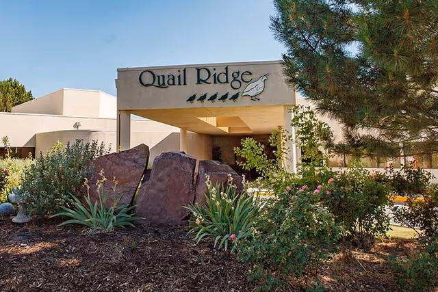 Entrance of the Quail Ridge building with a porte-cochere, sign and landscaped rocks and plants in the foreground.