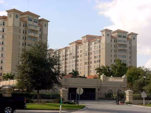 Large beige senior living building with gated entrance and greenery.
