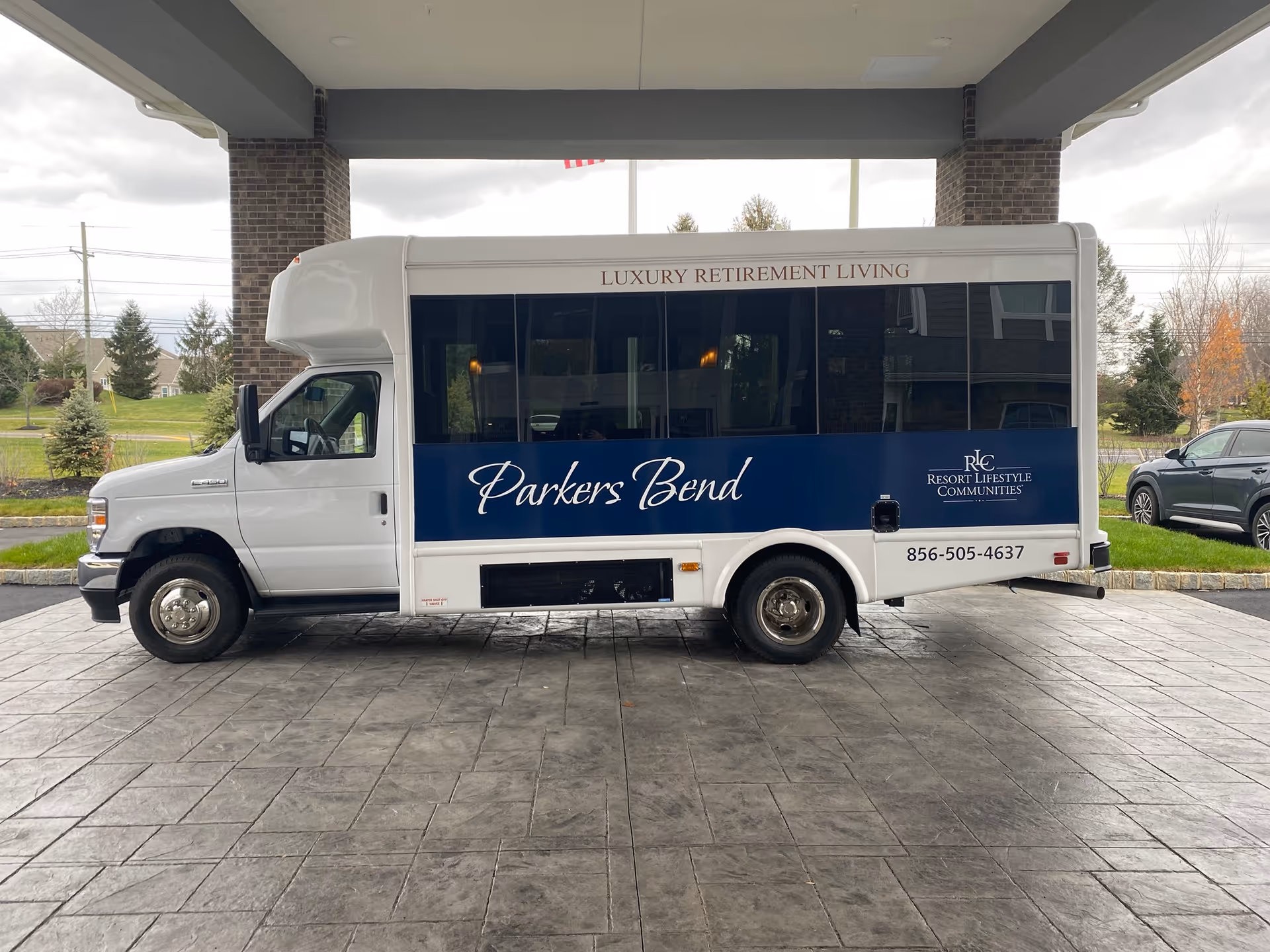 A white shuttle bus with 'Parkers Bend' and 'Luxury Retirement Living' branding parked under a covered entrance at the retirement community.