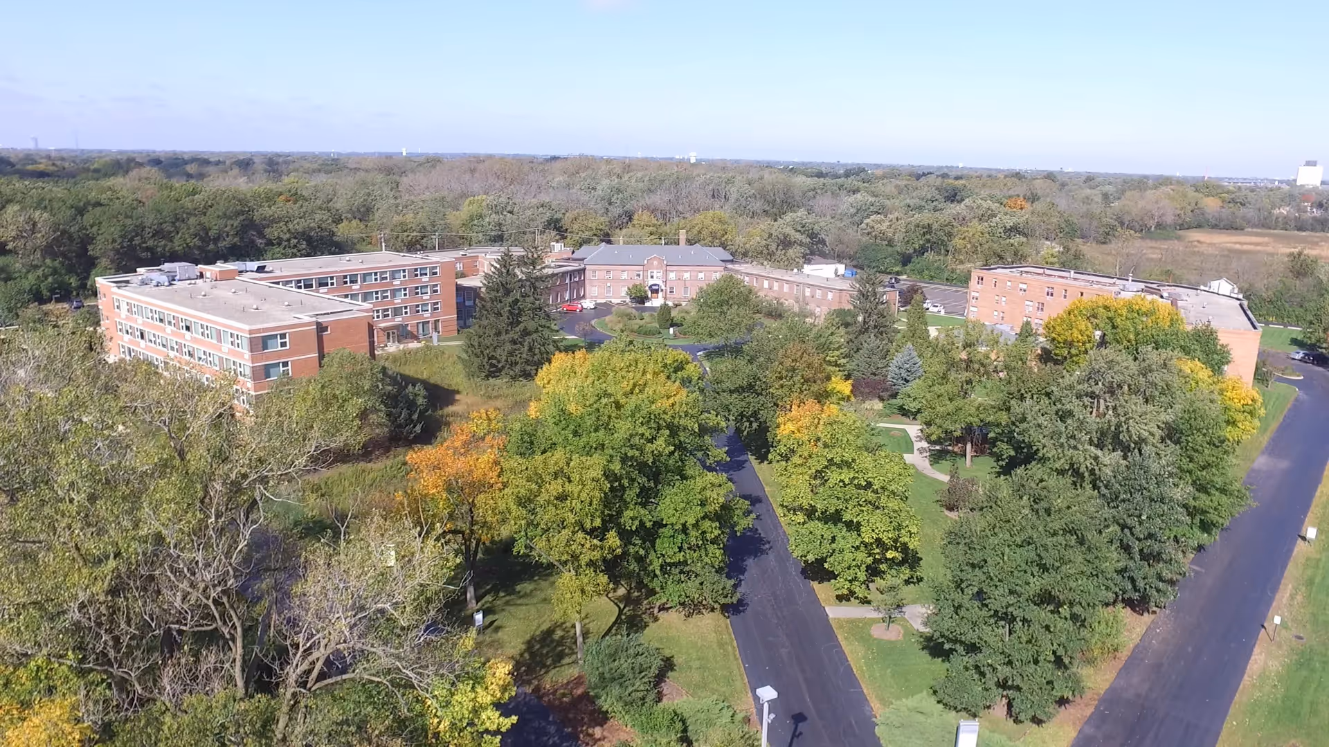 Aerial view of Cantata Adult Life Services a CCRC showing multiple connected brick buildings surrounded by trees and greenery with paved roads leading to the facility.