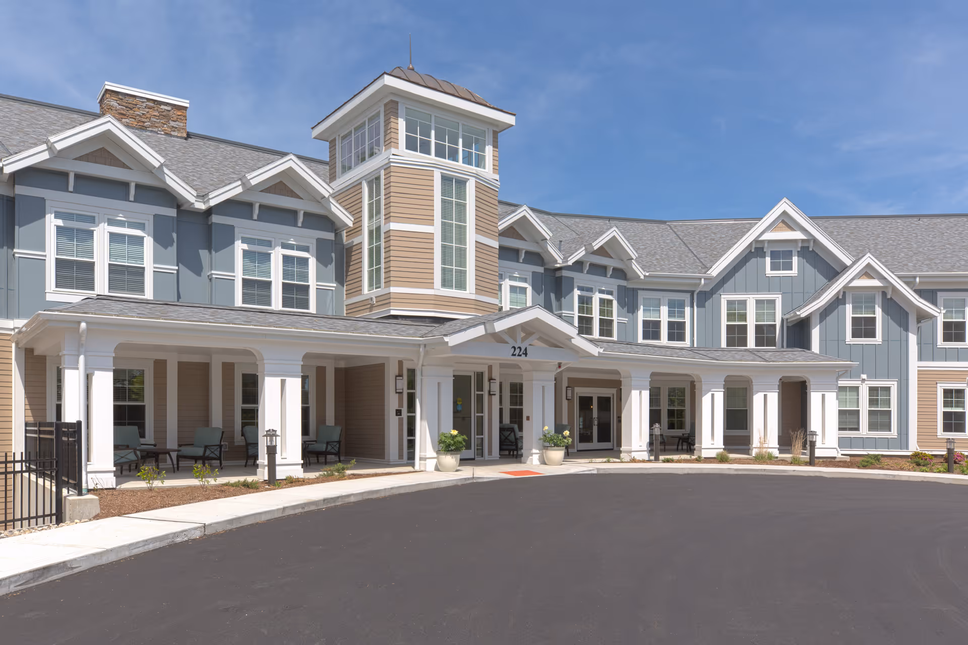 Exterior view of a senior living facility named The Residence at Vinnin Square, showing a large building with multiple windows, a covered entrance with white columns, and a paved driveway under a clear blue sky.