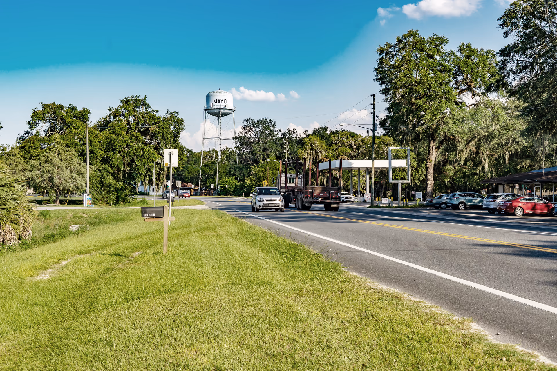 View of a road with a water tower in the background and vehicles parked along the roadside.