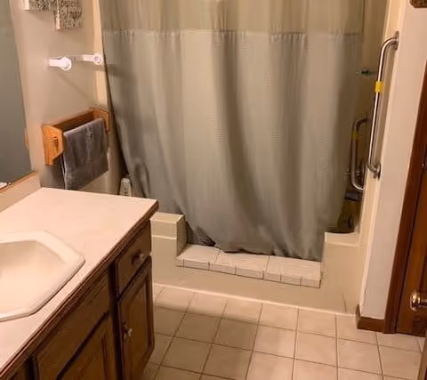 Small bathroom with a vanity sink and cabinet, tiled floor, and a shower with a curtain and grab bar.