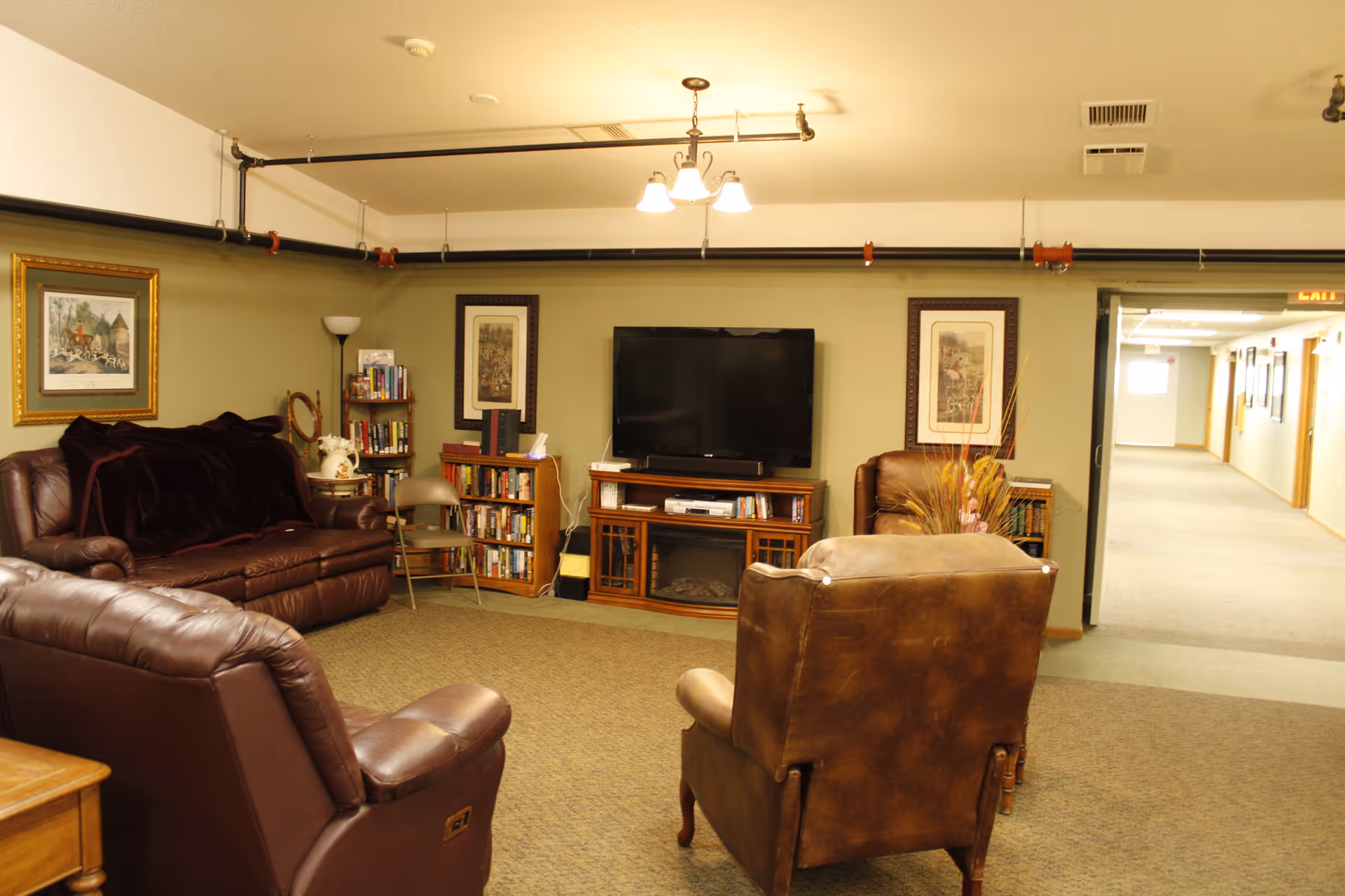 Cozy common living room with leather chairs and sofas facing a television, bookshelves, and framed artwork.