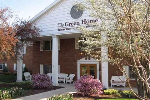 Front view of The Green Home senior living facility with white columns and blooming trees.