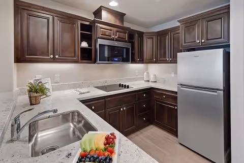 Modern kitchen with dark wood cabinets, stainless-steel appliances, light stone countertops, a sink, and a fruit platter on the counter.