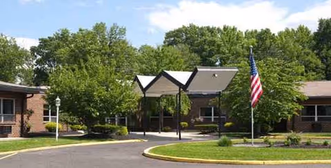 Exterior view of a Statesman Health and Rehabilitation Center with a driveway, flag, and trees.