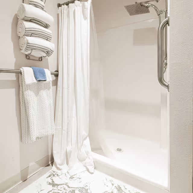 Walk-in shower with a white curtain, rain showerhead, wall-mounted grab bar, and neatly folded towels on a rack.