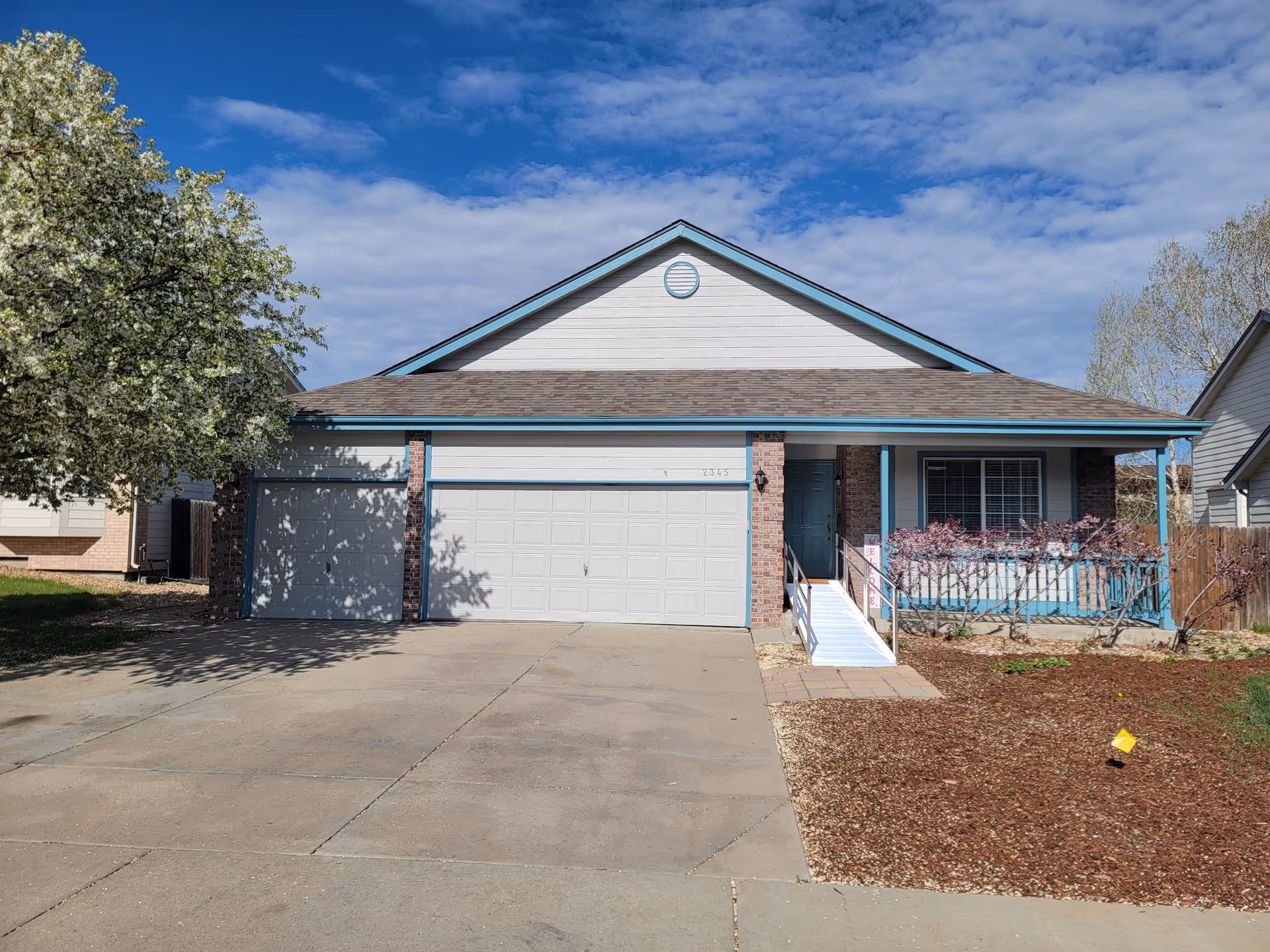 Front exterior of a single-story house with a two-car garage, driveway, and a small porch with a ramp.