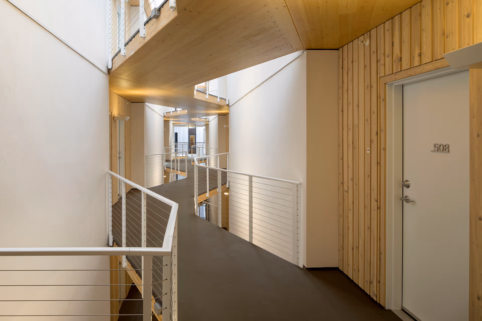 Interior corridor with suspended walkways, white metal railings, light wood-paneled walls and a door numbered 503.