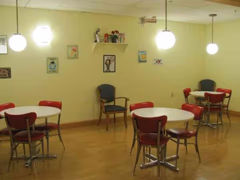Bright communal dining area with round tables, red chairs, and wall decor.